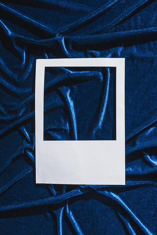 top view of empty white photo frame on blue velour cloth