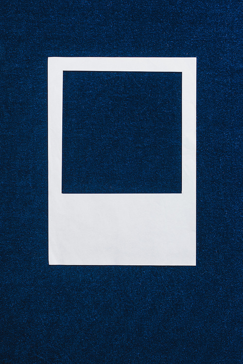 top view of white empty photo frame on blue textured background