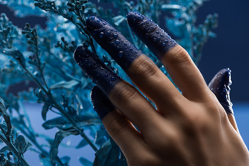 close up view of female hand with wet painted fingers near blue plant