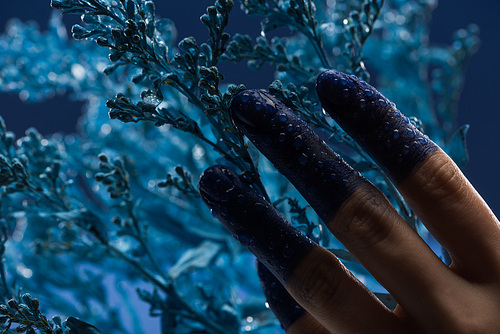 close up view of female hand with wet painted fingers near blue plant