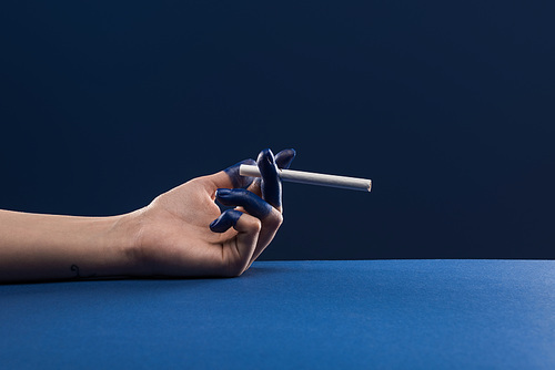 cropped view of female hand with painted fingers holding cigarette isolated on blue