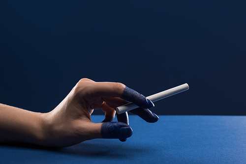cropped view of female hand with painted fingers holding cigarette isolated on blue