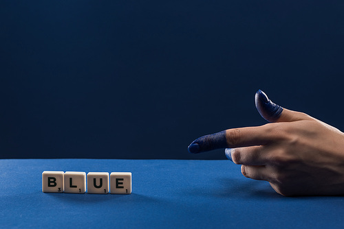 cropped view of female hand with painted fingers pointing at cubes with blue lettering isolated on blue