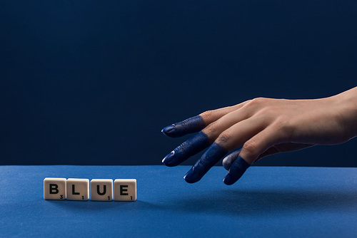 cropped view of female hand with painted fingers near cubes with blue lettering isolated on blue