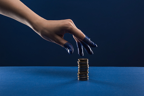 cropped view of female hand with painted fingers touching coins isolated on blue