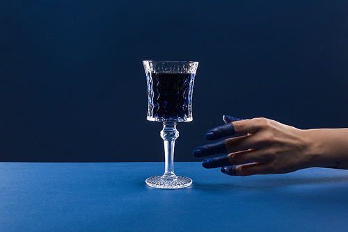 cropped view of female hand with painted fingers near faceted glass with drink isolated on blue