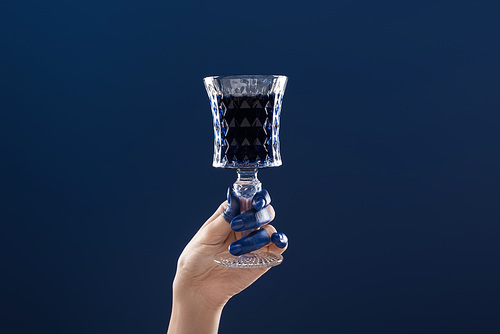 cropped view of female hand with painted fingers holding faceted glass with drink isolated on blue