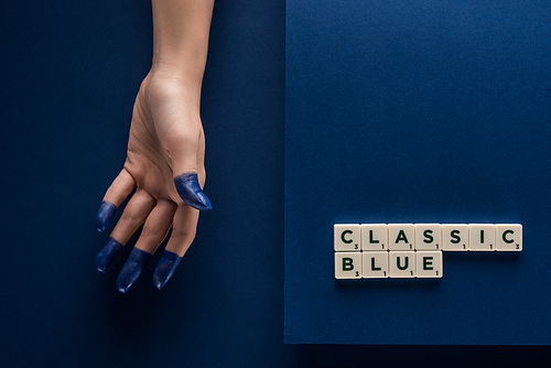 cropped view of woman with painted fingers near classic blue lettering on cubes on blue background