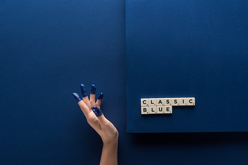 cropped view of woman with painted fingers near classic blue lettering on cubes on blue background