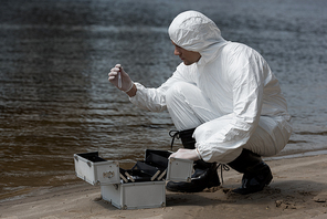 water inspector in latex gloves and protective costume opening inspection kit on sandy coast