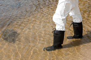 cropped view of water inspector in protective costume and boots standing in river