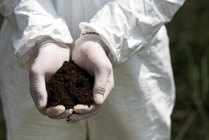 partial view of ecologist in latex gloves holding handful of soil