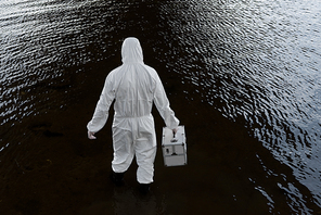 back view of water inspector in protective costume holding inspection kit in river