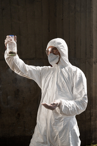 ecologist in protective costume and respirator holding bottle with soil sample