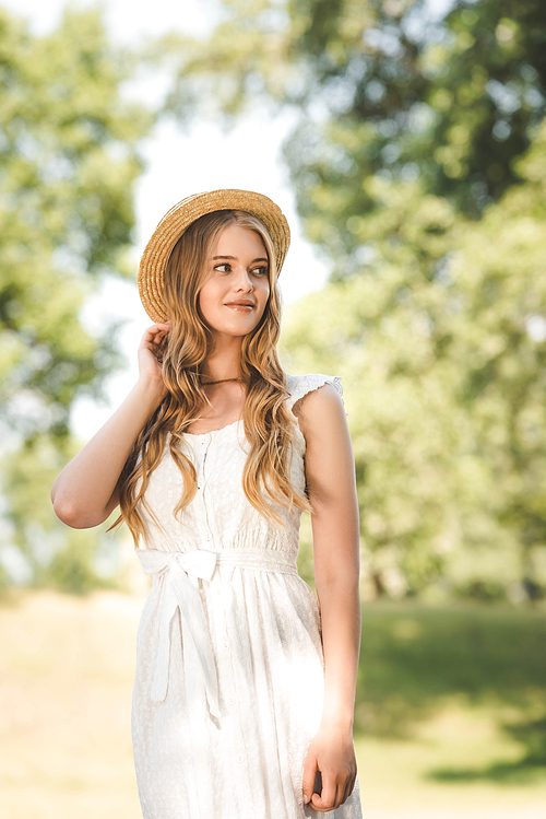 beautiful girl with straw hat standing on meadow and looking away