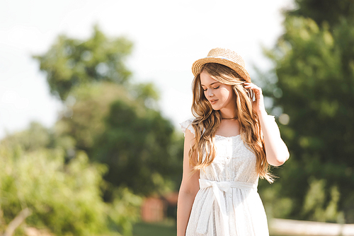 beautiful girl in white dress touching straw hat and looking down