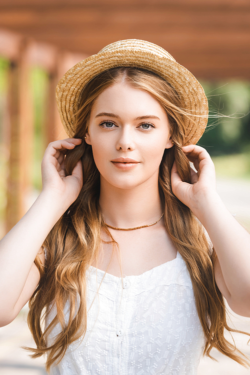 portrait shot of beautiful girl in straw hat touching hair while