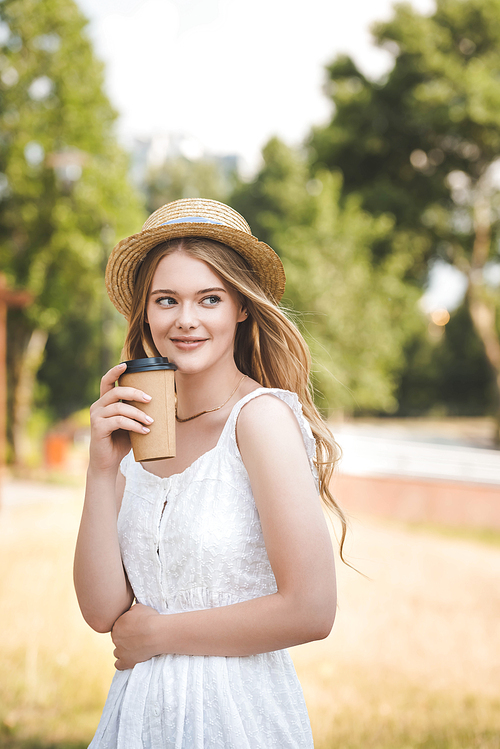 beautiful girl in white dress and straw hat holding paper coffee cup, smiling and looking away