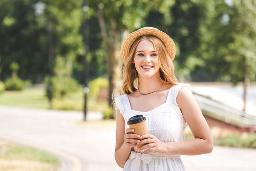 beautiful girl in white dress and straw hat holding paper cup, smiling and looking away