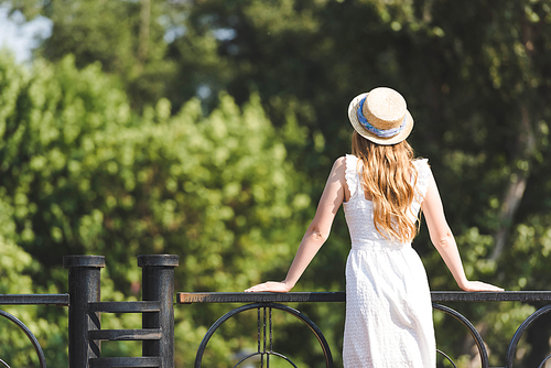 back view of girl in white dress and straw hat leaning on handrail