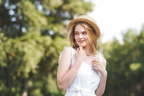 selective focus of beautiful girl in straw hat and white dress looking away