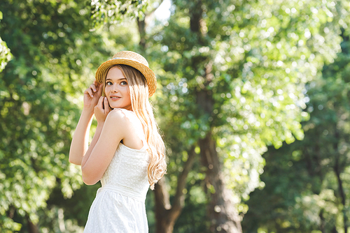 beautiful young girl in white dress and straw hat smiling and looking away