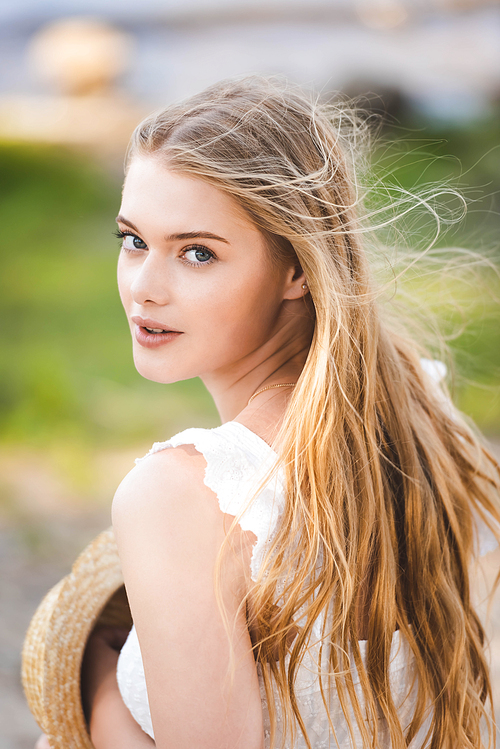 portrait shot of beautiful girl in white dress holding straw hat and 