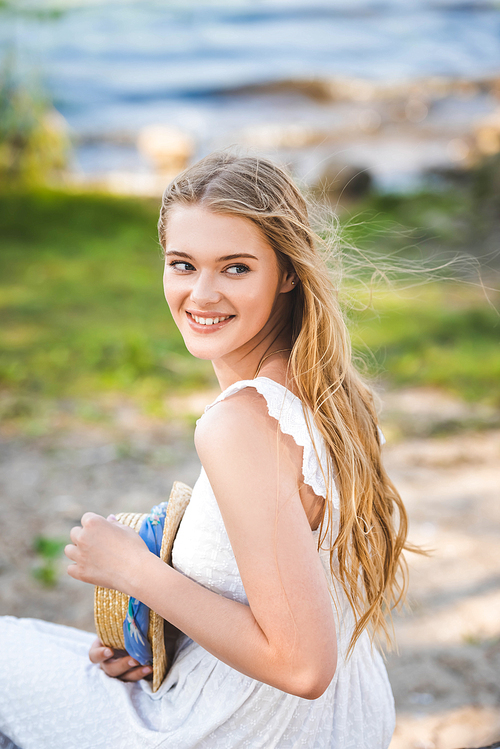 portrait shot of beautiful girl in white dress holding straw hat, smiling and looking away