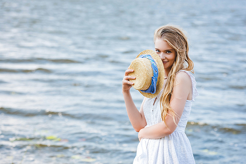 beautiful girl holding straw hat near face, smiling and 