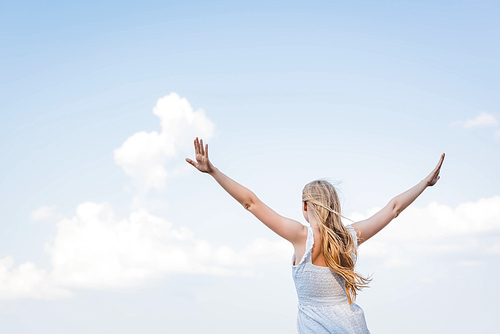 back view of girl in white dress standing with hands in air