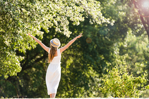 back view of girl in white dress walking in park with hands in air