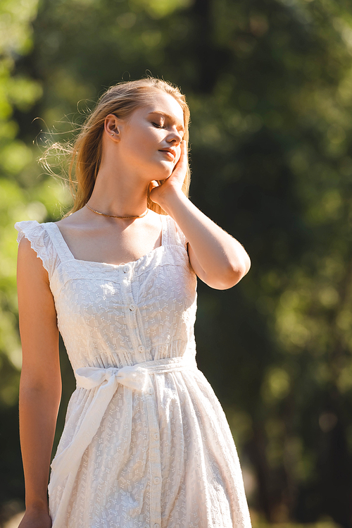 beautiful girl in white dress standing on meadow with closed eyes