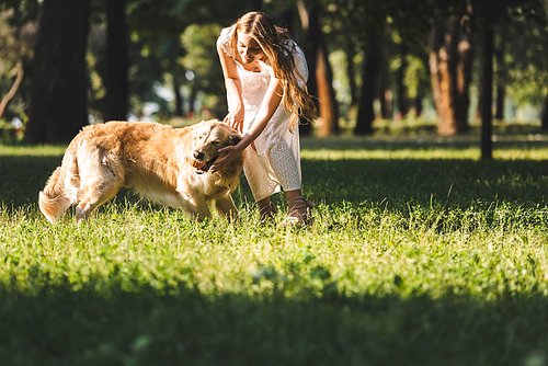 full length view of beautiful young girl in white dress playing ball with golden retriever on meadow