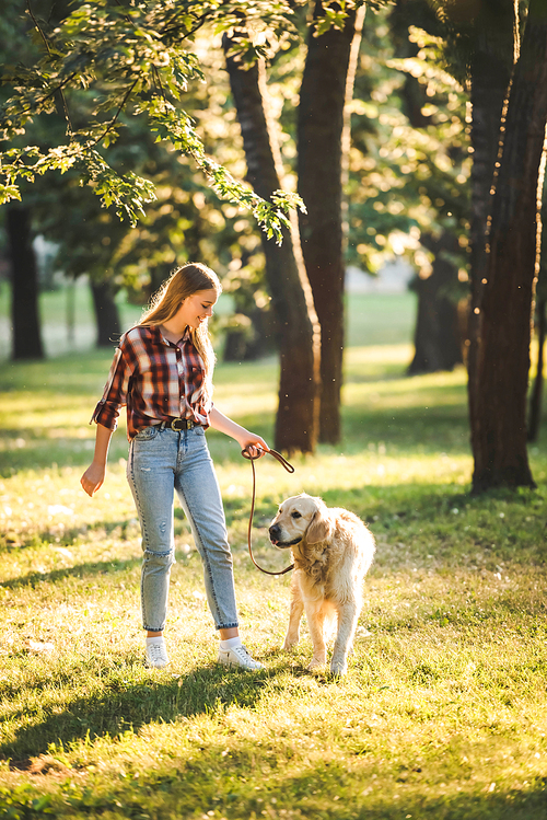 full length view of girl in casual clothes walking with golden retriever on meadow