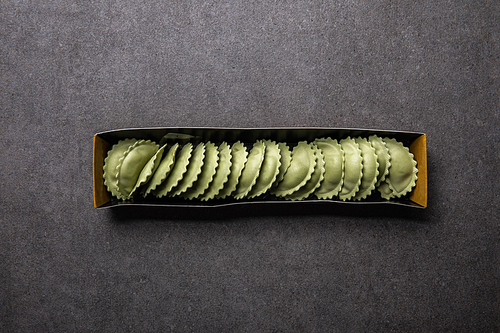 top view of green raw ravioli in cardboard box on grey textured surface