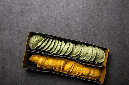 top view of green and yellow raw ravioli in cardboard box on grey textured surface