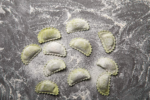 top view of raw green ravioli with flour on grey textured surface