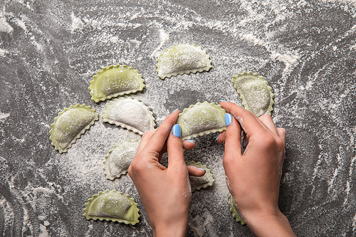 cropped view of woman holding green ravioli with flour