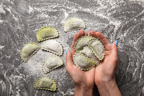 cropped view of woman holding green raw ravioli in hands