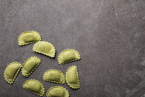 top view of green raw ravioli on grey textured surface with copy space