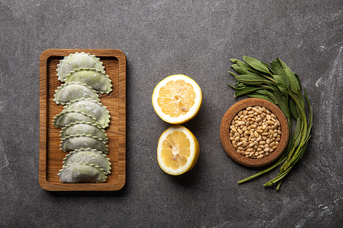 served on wooden board green ravioli with flour near bowl with seeds, lemon halves and herb