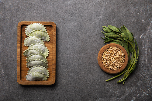 served on wooden board green ravioli with flour near bowl with seeds and herb