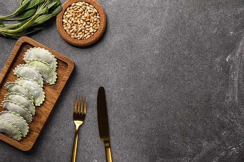 served on wooden board green ravioli with flour near bowl with seeds, herb and cutlery