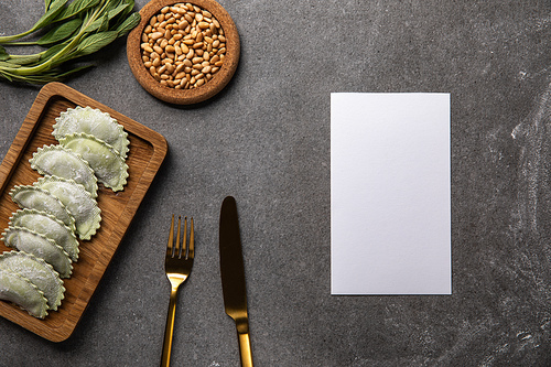 served on wooden board green ravioli with flour near bowl with seeds, herb, cutlery and empty card