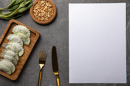 served on wooden board green ravioli with flour near bowl with seeds, herb, cutlery and blank card