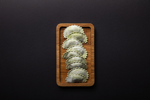 top view of raw green ravioli with flour on wooden board isolated on black