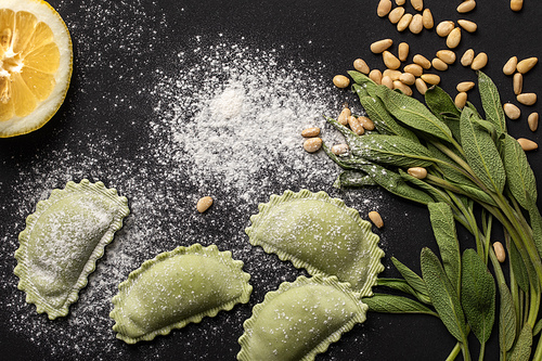 top view of raw green ravioli with pine nuts, flour, green sage and lemon