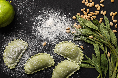 green raw ravioli, pine nuts, herb, lime and flour on black background