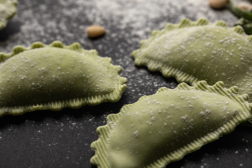 close up view of green raw ravioli with flour on black table