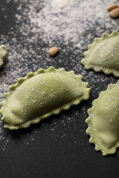 close up view of green ravioli with flour on black table